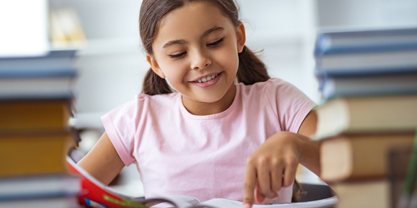 Menina de uns 7 a 8 anos, sorrindo e lendo