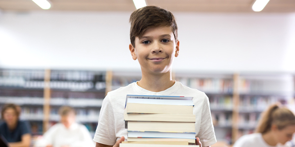 Menino do ensino fundamental sorrindo com livros na mão