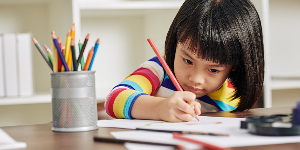 Menina sentada desenhando com porta lápis cheio de lápis de cor