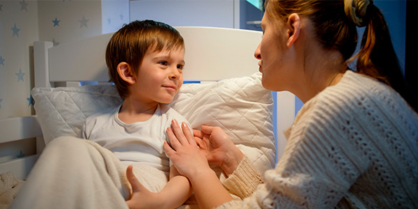 Menino sentado na cama conversando com a mãe